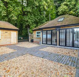 An outdoor courtyard with two wooden buildings surrounded by trees at Dreamwood Lodge in Keston near Leaves Green