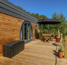 An outdoor wooden deck with a table and chairs under a black umbrella and potted plants at The Hideaway Pod Rhoslan near Criccieth