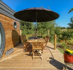 A wooden deck with a table, chairs, and a large umbrella outside a cabin at The Hideaway Pod in Rhoslan near Criccieth