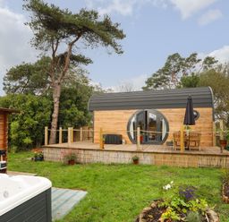 A wooden pod with circular windows on a raised deck with a table and chairs and a garden with a hot tub at The Hideaway Pod in Rhoslan near Criccieth