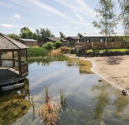 A lakeside with a wooden gazebo a sandy shore and several cabins in the background at Parkers Place Carnforth