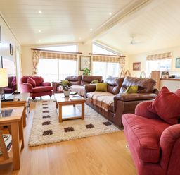 A living room with red and brown sofas a wooden coffee table a patterned rug and large windows at Tanqueray Lodge in Kenwick near Louth