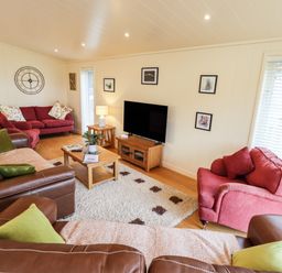 A living room with red and brown sofas a coffee table a television and a wall clock at Tanqueray Lodge in Kenwick near Louth
