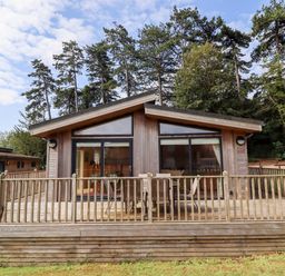 A wooden cabin with a deck and outdoor table and chairs surrounded by trees at Tanqueray Lodge Kenwick near Louth
