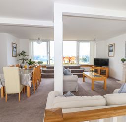 A living and dining area with beige sofas a wooden dining table and chairs a coffee table and a fireplace at Apartment at Morningside Hotel in Torquay
