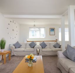 A living room with three sofas a wooden coffee table with flowers a decorative wall clock and a window at Apartment at Morningside Hotel in Torquay