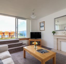A living room with a sofa coffee table and television next to sliding glass doors leading to a balcony at Apartment at Morningside Hotel in Torquay
