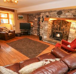 A living room with leather sofas a red armchair a stone fireplace with a wood burner a television and a window with curtains at Pant Teg Farm in Carmarthen