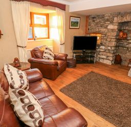 A living room with brown leather sofas cushions a rug a TV and a stone wall at Pant Teg Farm in Carmarthen
