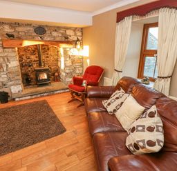 A living room with a stone fireplace wood stove a brown leather sofa and a red armchair at Pant Teg Farm in Carmarthen