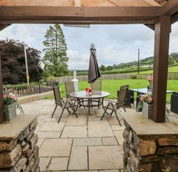 An outdoor patio with a round table and chairs under a wooden pergola at Pant Teg Farm in Carmarthen