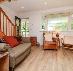 A living room with a sofa, armchair, wooden chair, side table with a lamp, and wooden staircase at Barleside in Dulverton