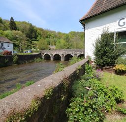 A river with a stone bridge and houses near a garden with plants and flowers at Barleside in Dulverton