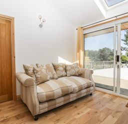 A beige striped sofa with patterned cushions next to a sliding glass door and wooden door on a wooden floor