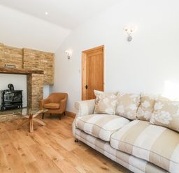 A living room with a striped sofa, armchair, glass coffee table, wood stove in a stone fireplace at Steel Works Farm in Gorsley
