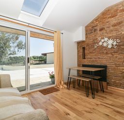 A room with a sofa, wooden table with benches, stone wall, sliding glass door, and skylight at Steel Works Farm in Gorsley