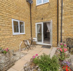 A small outdoor patio with a table and two chairs flowers in stone planters and a metal chair at The Cornerstone in Bourton-On-The-Water