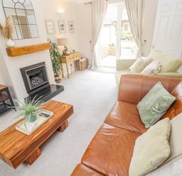 A living room with leather and fabric sofas a wooden coffee table a fireplace and glass doors at The Cornerstone in Bourton-On-The-Water