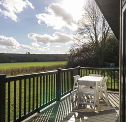 An outdoor deck with a white table and four chairs overlooking a grassy field at Manor Farm Lodge in Bowerchalke