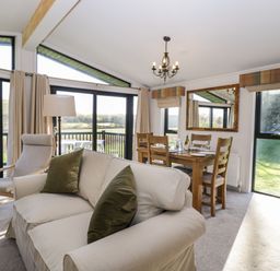A living room with a sofa and armchair next to a dining table with chairs and a large mirror at Manor Farm Lodge in Bowerchalke