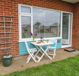 A small outdoor patio area with a white table and two chairs set with breakfast at 12 Siesta Mar in Mundesley