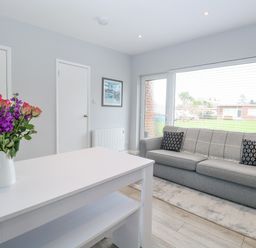 A room with a gray sofa with two pillows a white table with flowers and a large window at 12 Siesta Mar in Mundesley