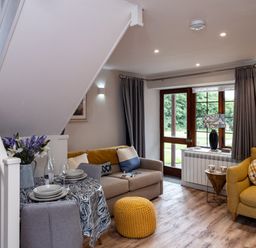 A living room with sofas a knitted footstool dining table under stairs and a door with curtains at The Snug in St Minver