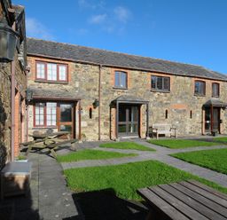 An outdoor area with stone cottages wooden benches and tables on grass at The Snug in St Minver