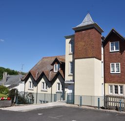 A residential building with cream and brown exterior walls and a tower structure under a clear blue sky at 1 Buckfields in Lyme Regis