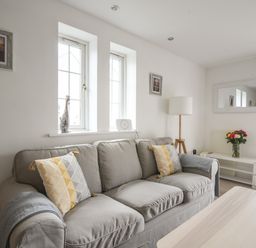 A living room with a grey sofa yellow and grey patterned pillows a floor lamp a large mirror and flowers on a table at 1 Buckfields in Lyme Regis