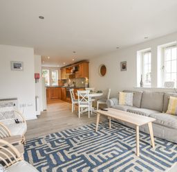 An open living room and kitchen with sofa, armchairs, dining table, and wooden cabinets at 1 Buckfields in Lyme Regis
