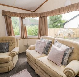 A sitting room with beige armchairs and sofa with cushions and curtains on windows at Grange Caravan in Llangollen
