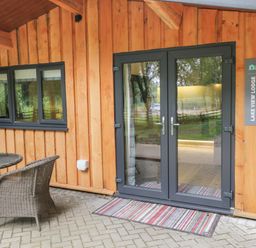 Wooden exterior with glass double doors and a window next to a round table and two wicker chairs at Lake View Lodge Wykeham near East Ayton