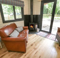 A room with a brown leather sofa and armchair wooden floor a stove and glass door at Lake View Lodge in Wykeham near East Ayton