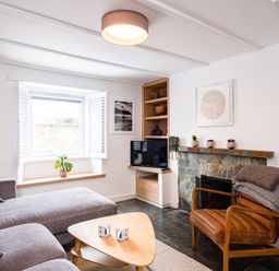 A living room with a gray sofa a wooden triangular coffee table a leather chair with blankets a stone fireplace a TV and a window at West Cottage in Rock