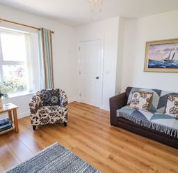 A living room with a sofa a patterned armchair a small wooden table and a painting of a sailboat at 4 The Cloisters in Bushmills County Antrim