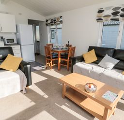 A living room with black sofas yellow and grey cushions a wooden coffee table and a dining table with four chairs at Pinecone Lodge - No 9 Felmoor Park near Felton
