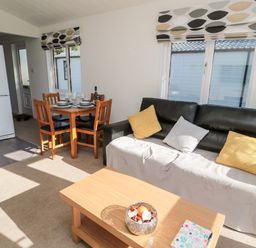 A living room with a black sofa and yellow and gray cushions near a wooden coffee table and dining table at Pinecone Lodge - No 9 Felmoor Park near Felton