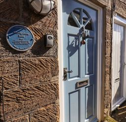 A blue front door with a sea creature door knocker and a blue plaque on a stone wall at Navigators Rest in Whitby