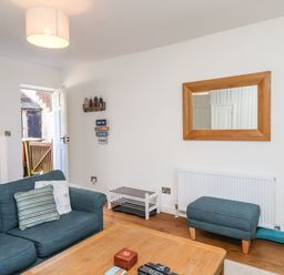 A living room with a blue sofa and ottoman a wooden coffee table a wall mirror and an open door at Navigators Rest in Whitby