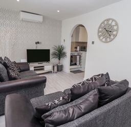 A living room with two sofas cushions television plant and wall clock at 19 Cherry Park in Chapel St Leonards
