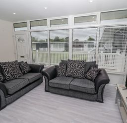 A living room with two sofas, a television on a stand, and windows with blinds at 19 Cherry Park in Chapel St Leonards
