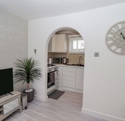 A living room with a television and plant next to an arched doorway leading to a kitchen with white cabinets at 19 Cherry Park in Chapel St Leonards
