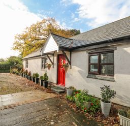 A single-story house with a red door and potted plants along the exterior at Burnt Oak Stables in Mynydd Isa