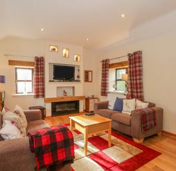 A living room with two sofas a wooden coffee table and a wall-mounted television at Burnt Oak Stables in Mynydd Isa