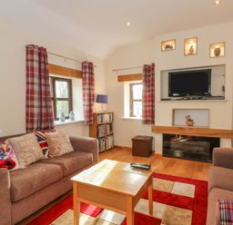 A living room with two brown sofas a wooden coffee table a wall-mounted TV and red plaid curtains at Burnt Oak Stables in Mynydd Isa