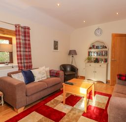 A living room with two sofas a coffee table a bookshelf and a window with red plaid curtains at Burnt Oak Stables in Mynydd Isa