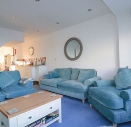 A living room with blue sofas a wooden coffee table and a round mirror on the wall at Sea View in Mevagissey