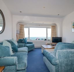A living room with blue sofas a coffee table a TV and a window with a sea view at Sea View in Mevagissey