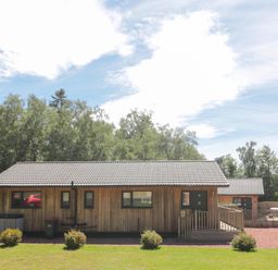 A wooden cabin with a tiled roof and small bushes in front at Lodge 32 in Otterburn